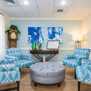 A modern waiting room with blue patterned chairs, abstract artwork, and a central ottoman.