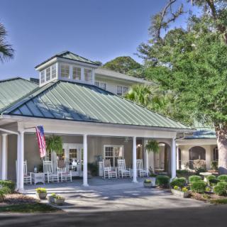 A building with a covered entrance and rocking chairs on the porch, surrounded by trees.