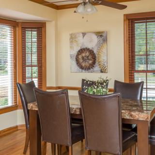 A cozy dining room featuring a wooden table with six leather chairs, surrounded by large windows and decorated with wall art.