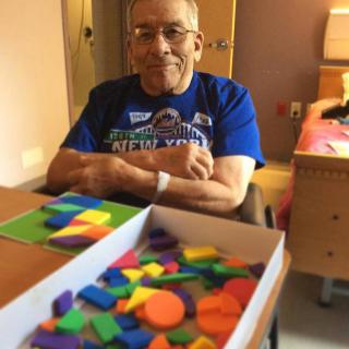 An elderly person smiling while sitting at a table with colorful puzzle pieces.
