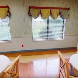 A dining area featuring tables, chairs, and windows with decorative curtains.