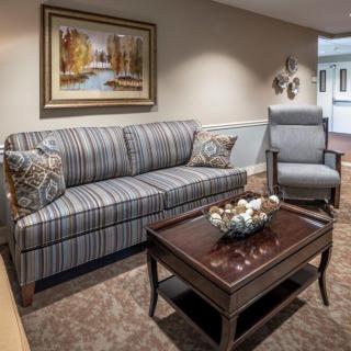A cozy living room setting featuring a striped sofa, a comfortable armchair, and a wooden coffee table adorned with decorative items.