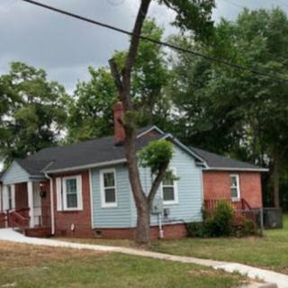 A suburban house with a brick exterior and a tree in the front yard on a cloudy day.