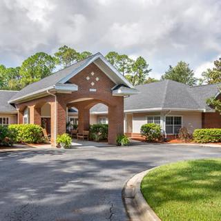 A welcoming entrance to a residential building with a landscaped driveway and surrounding trees.