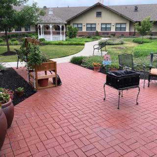 A peaceful garden with a brick patio, outdoor furniture, and a gazebo in the background.