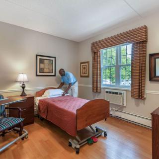A well-decorated nursing home room with a single hospital bed and a caretaker tidying up.