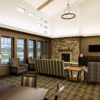 A modern living room with comfortable seating around a stone fireplace, featuring large windows and contemporary lighting.