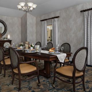 A spacious dining room with a classic wooden table set for dinner, surrounded by elegant chairs and adorned with a chandelier.