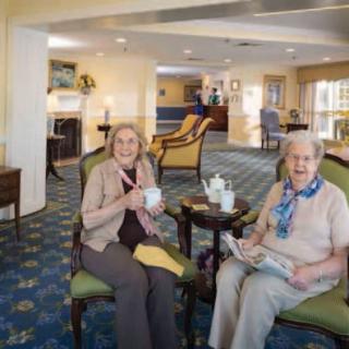 Two senior women enjoying tea and conversation in a comfortable living room setting.