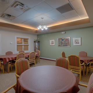 A cozy dining room with several round tables and chairs, warmly lit with ceiling lights.