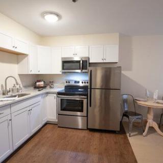 A modern kitchen with stainless steel appliances, white cabinets, and wood flooring.