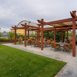 An outdoor seating area with a wooden pergola and patio furniture, set in a landscaped garden.