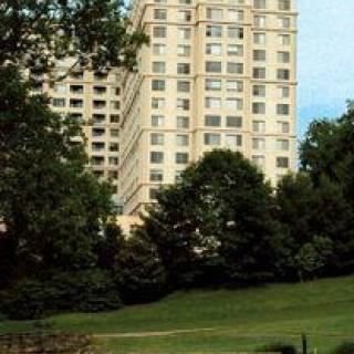 A view of a high-rise building surrounded by trees and a grassy park area.