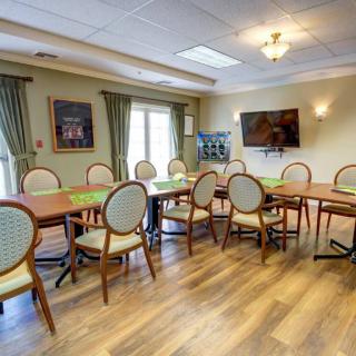 A dining room with tables and chairs arranged on a wooden floor, featuring curtains and wall art.