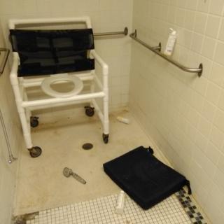 An accessible shower area with a wheelchair and safety handrails.