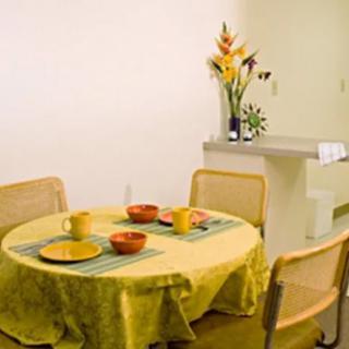 A cozy dining area with a round table set for breakfast, featuring a yellow tablecloth and a vase of flowers in the background.