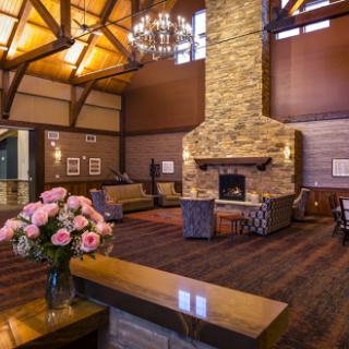 A cozy lobby featuring a stone fireplace, wooden beams, and comfortable seating arrangements, complemented by fresh flowers.