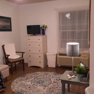 A cozy living room with furniture, including a chair, dresser, and TV, complemented by a decorative rug and lamp.