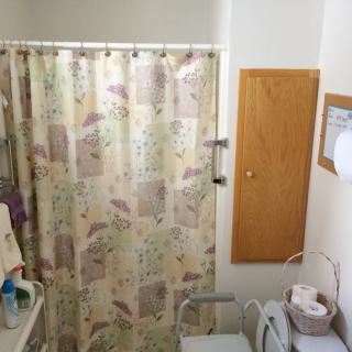 A small bathroom with a floral shower curtain, wall cabinet, and various toiletries.