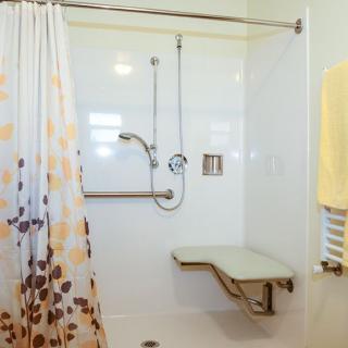 An accessible bathroom featuring a shower with a foldable chair, grab bars, and a decorative shower curtain.