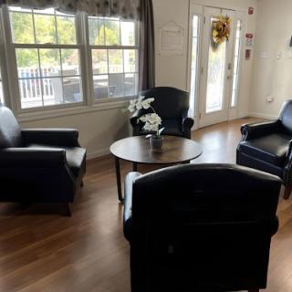 A cozy living room setup featuring black chairs and a circular table, illuminated by natural light.