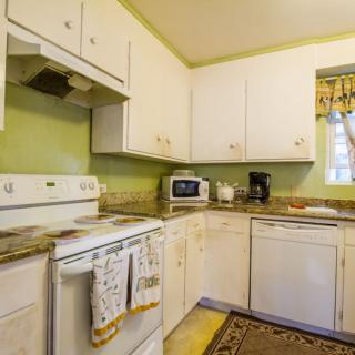 A cozy kitchen with white cabinets and green walls, featuring modern appliances including an oven, microwave, coffee maker, and dishwasher.