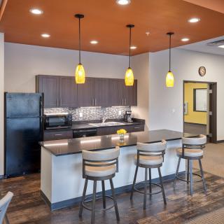 A modern kitchen interior with an island and bar stools, featuring pendant lighting and appliances.