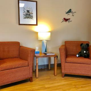 A cozy living room corner featuring orange chairs, a side table with a lamp, and playful wall art.