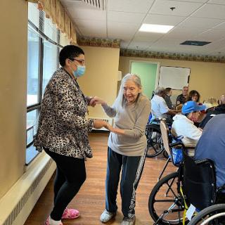 A joyful moment between a caregiver and an elderly resident, dancing together in a nursing home.
