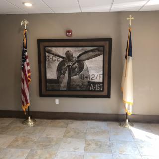 This image shows an interior wall with a prominent painting flanked by an American flag and a church flag.
