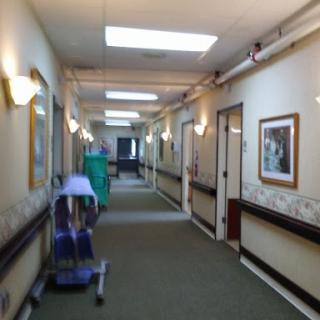 A well-lit hallway in a healthcare facility, featuring doors and framed artwork along the walls.