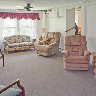 A cozy living room featuring a floral sofa, two plush armchairs, and bright natural lighting from a large window.