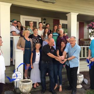 A group of people gathered on a porch for a ribbon-cutting ceremony.