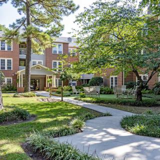 A scenic view of a brick residential building surrounded by lush greenery and a paved pathway.