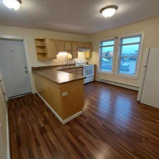 A modern kitchen with wood flooring, ample cabinetry, and large windows.