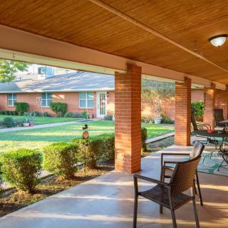 A sunny patio with chairs and a table overlooks a well-maintained garden and brick building.