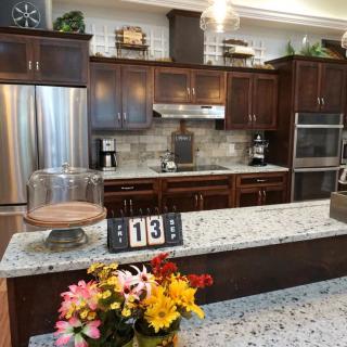 A modern kitchen with dark wood cabinets, granite countertops, and stainless steel appliances. A flower arrangement and cake display add a touch of elegance.