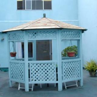 A blue wooden gazebo with lattice panels and potted plants, situated outdoors.