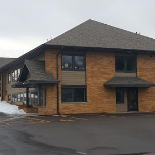 A two-story residential building with a brick exterior and gray roof, surrounded by snow.