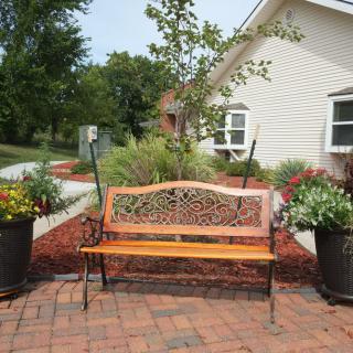 A decorative bench surrounded by potted plants on a brick patio.