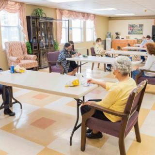 A group of senior citizens seated at tables in a community center, engaging in activities.