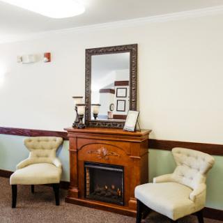 A cozy living room setup featuring a wooden fireplace, decorative mirror, and upholstered chairs.