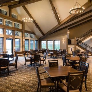 A spacious dining room with wooden beams, large windows, and elegant chandeliers.
