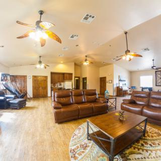 A spacious living room with leather sofas, ceiling fans, and wooden flooring.