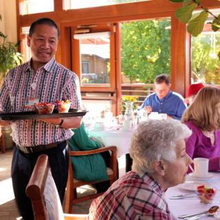 A waiter serving drinks to customers at a bright and sunny restaurant.