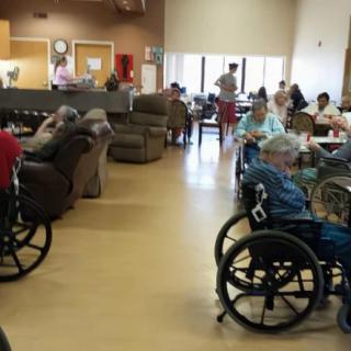 Elderly residents in wheelchairs gather in a common area of a nursing home.