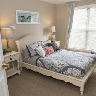 A cozy and stylish bedroom featuring a bed with decorative pillows, bedside lamps, and natural light from the window.