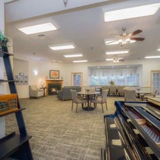 A cozy lounge area with comfortable seating, a piano, bookshelves, and a fireplace.