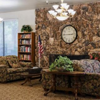 A cozy living room with a stone wall, featuring a bookshelf, clock, and furniture.