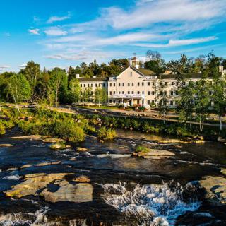 A scenic view of a river cascading over rocks with a picturesque building in the background under a clear blue sky.